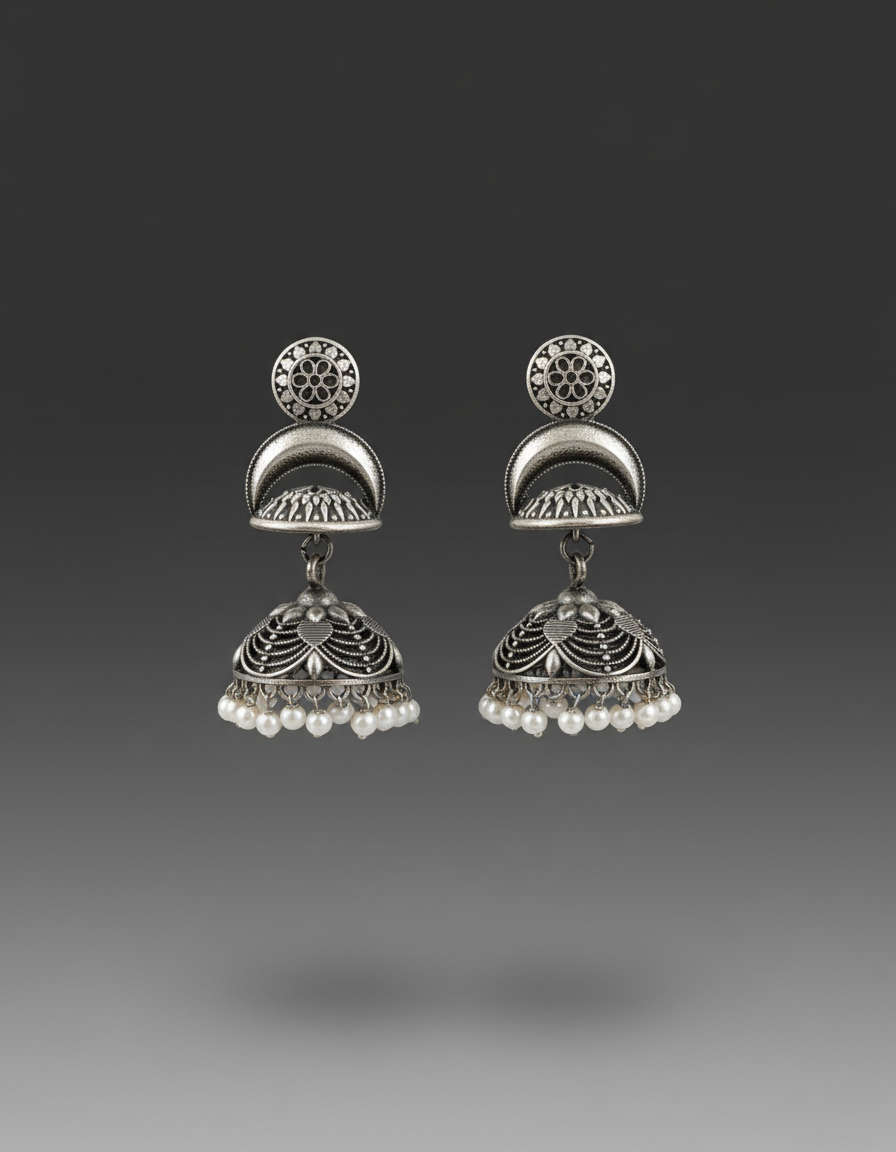 A pair of traditional Indian silver jhumka earrings with intricate filigree work and small white pearl bead drops, shown against a dark gray gradient background.