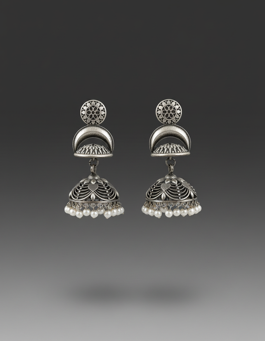 A pair of traditional Indian silver jhumka earrings with intricate filigree work and small white pearl bead drops, shown against a dark gray gradient background.